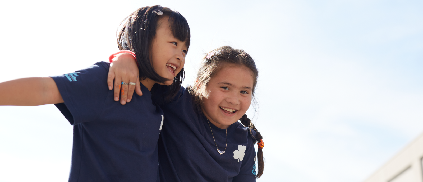 Two Spark-aged girls in uniforms huging in the outdoors